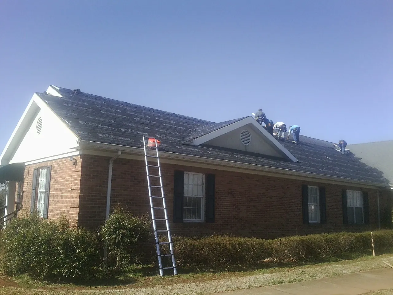 Crew tearing shingles off a brick ranch roof with a ladder set — Emergency Roof Repair work by our crew in Grantham