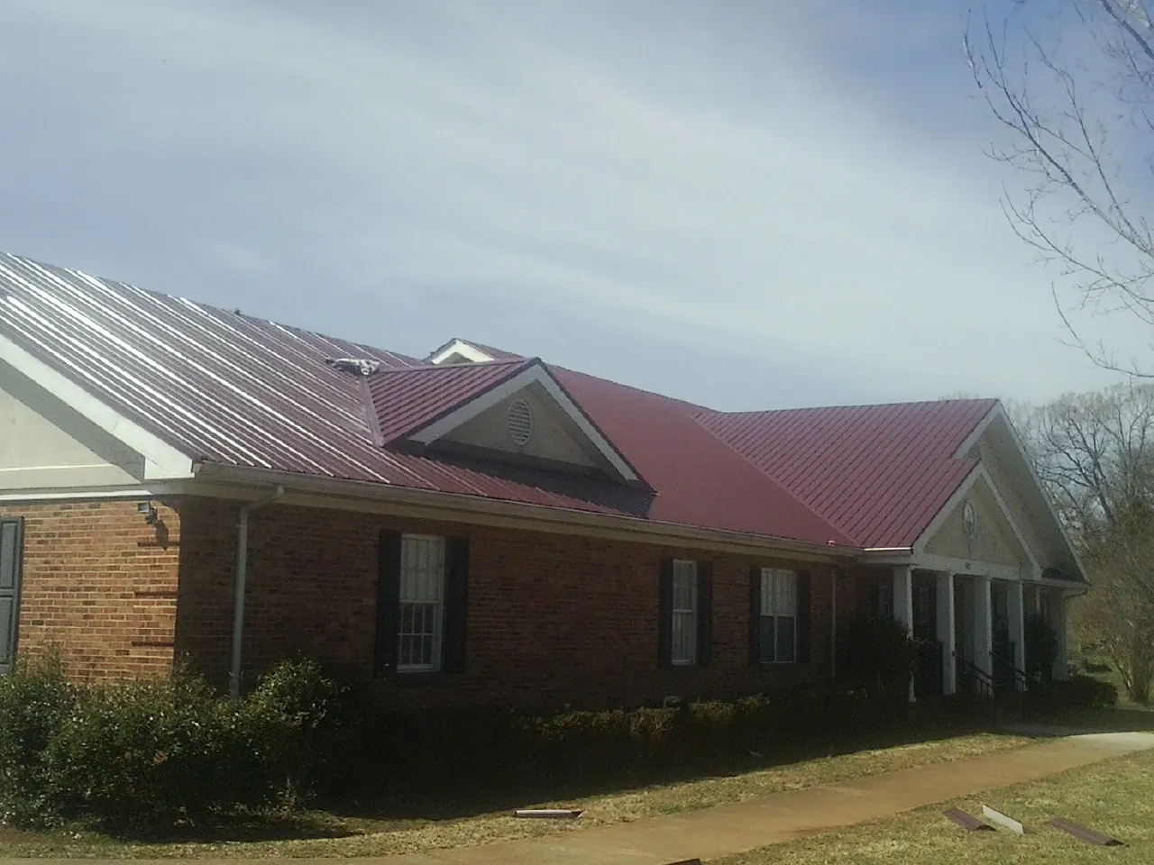 Red metal roof with gabled entries on a long brick building, from a Hail Damage Roof Repair job in Grantham
