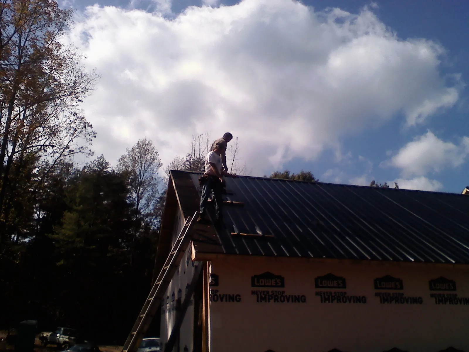 Roofer fastening dark metal panels high against a cloudy sky, from a Roof Inspection job in Grantham