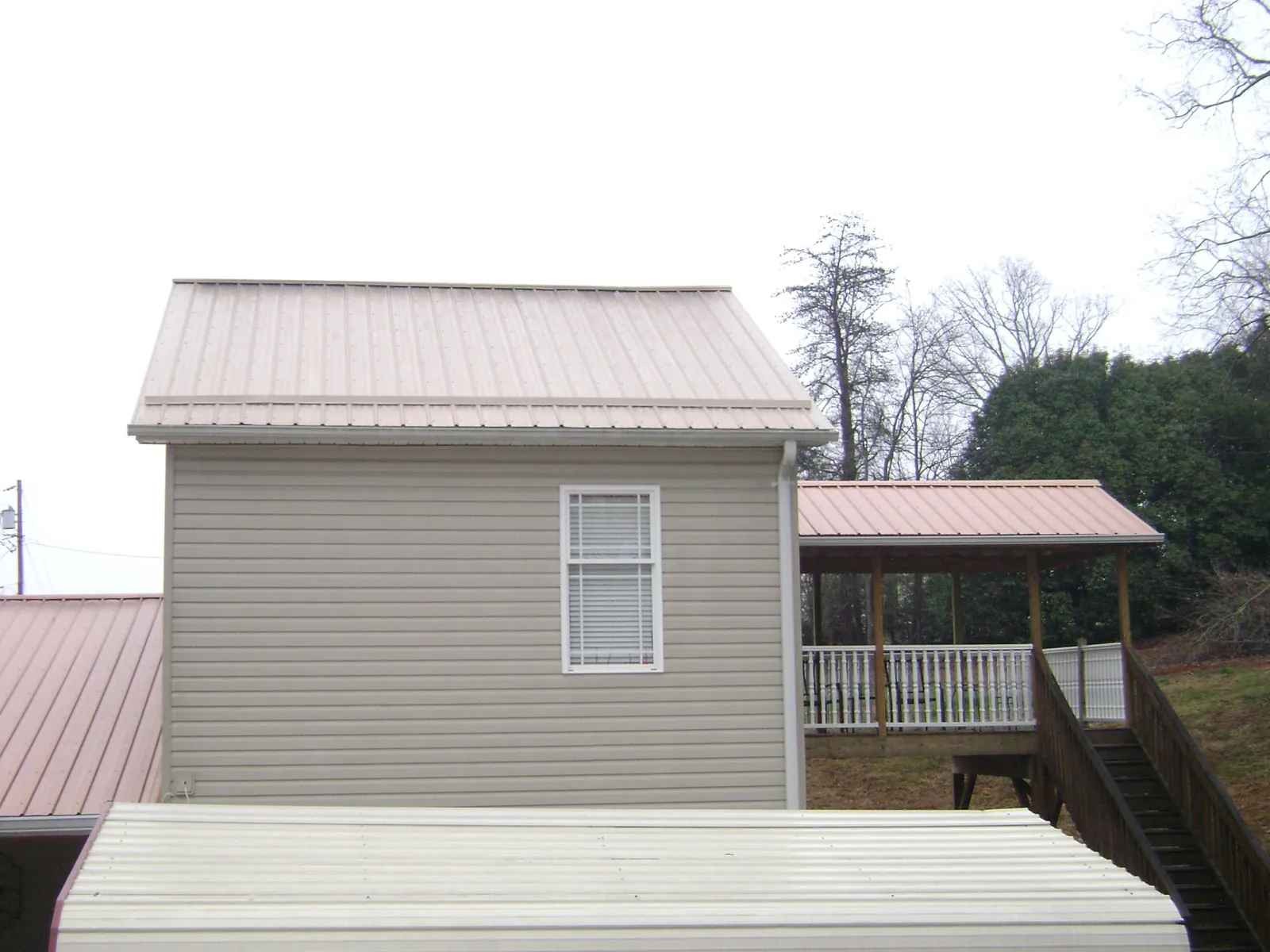 Tan metal roofs on a two story addition and attached porch, from a Roof Replacement job in Grantham